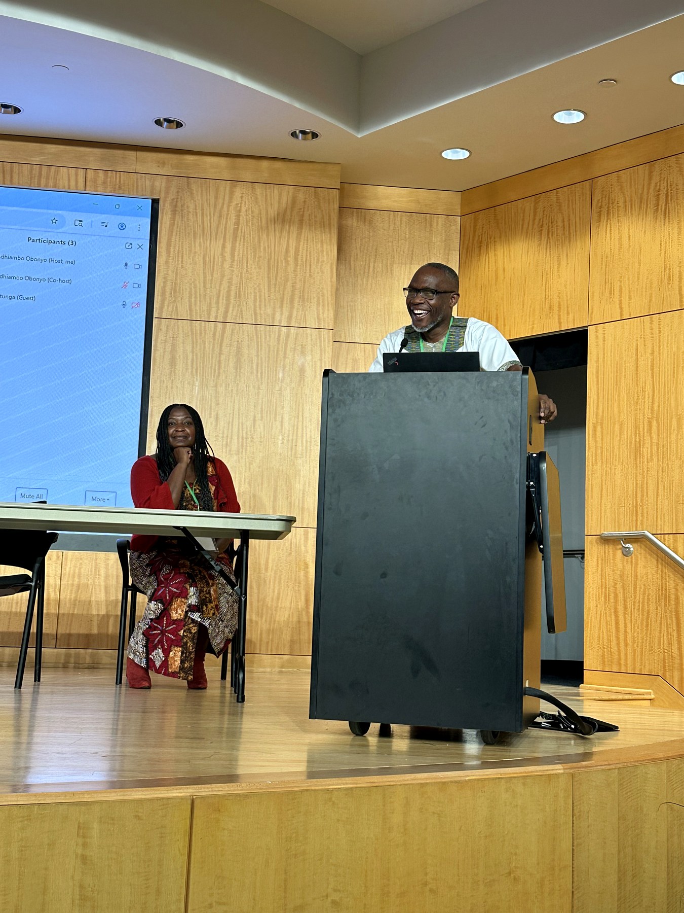 Patrick Mose moderating a hybrid session from a podium while a panelist listens on stage