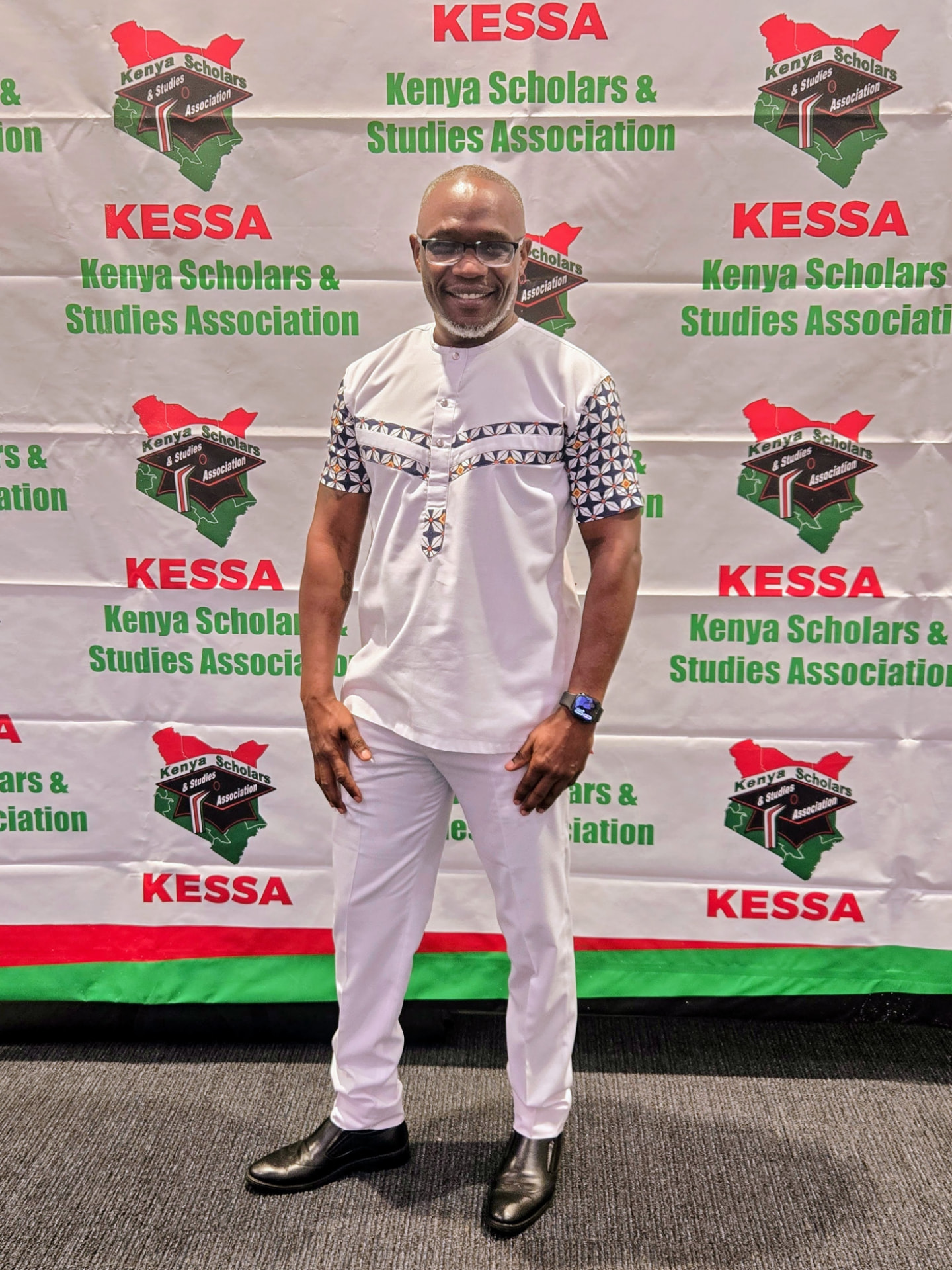 Patrick Mose standing in front of a Kenya Scholars and Studies Association conference backdrop